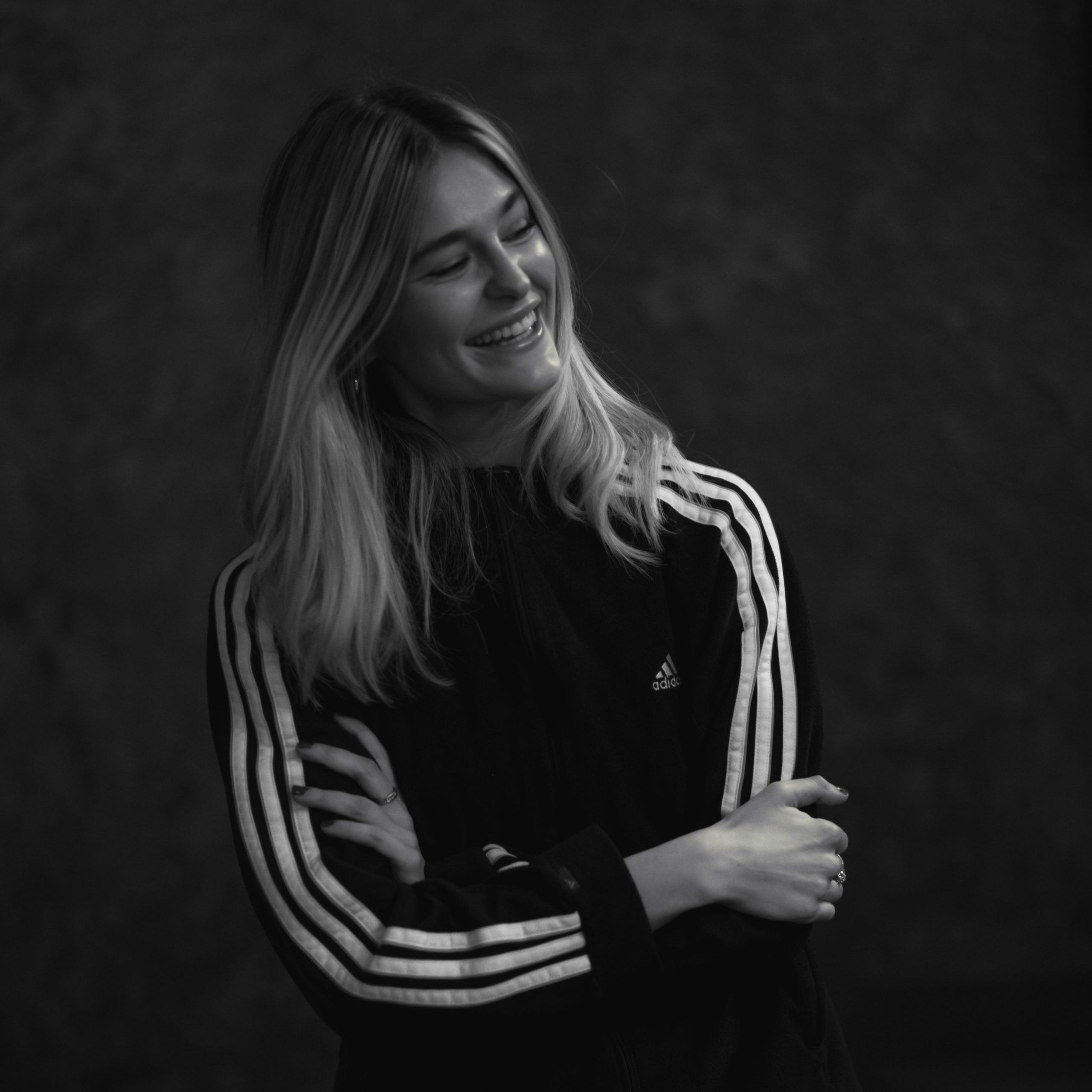 Portrait photograph of new Northern Visuals Employee, Elizabeth Wright laughing at work - black background. Liz is wearing an Adidas top.